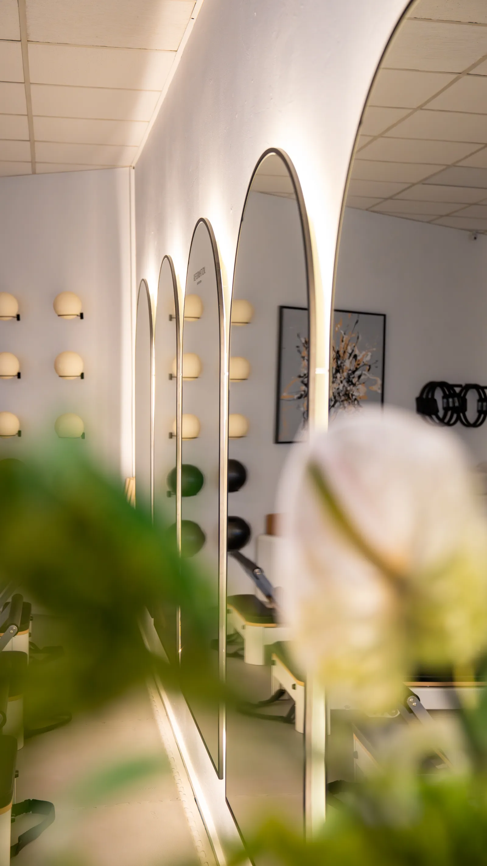 Bogenspiegel und Wandregale im REFORMOTION Studio, davor unscharfe Blüten